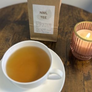 Tüte NWL-Tee mit einer Tasse Tee und Kerze auf einem Holztisch